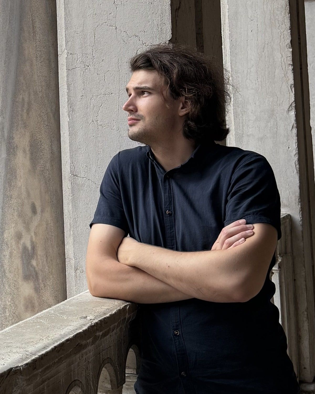 Ivan naslonjen na kamenu ogradu lođe u Veneciji, prekriženih ruku, gleda u stranu.